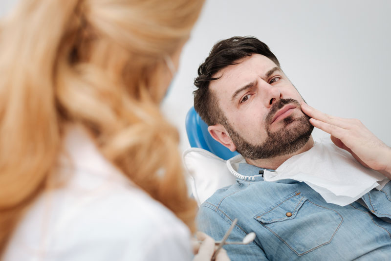 an image of a patient at a dental office lying on a patient chair talking to his oral surgeon about his wisdom tooth pain before his wisdom tooth removal procedure.