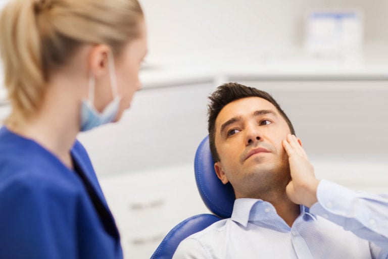 a patient holding his hurting jaw as an oral surgeon determines if he is a candidate for a wisdom tooth removal.