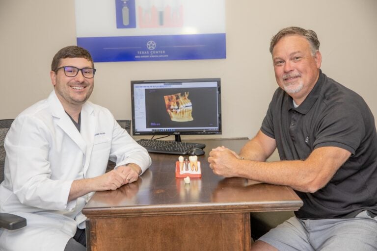 Dr. Vickers smiling with a patient, with a All- On-4 dental implant model between them.