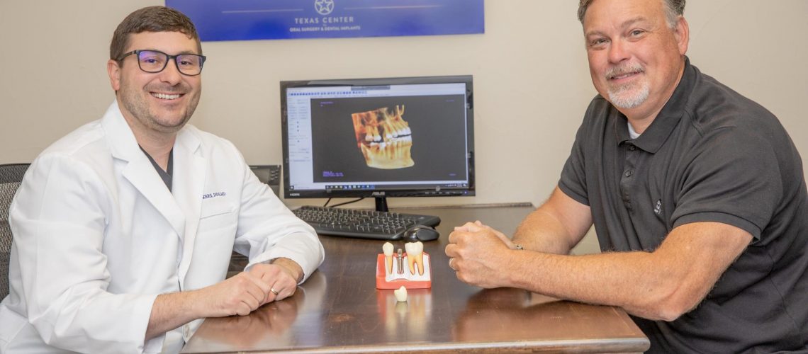 Dr. Vickers smiling with a patient, with a All- On-4 dental implant model between them.