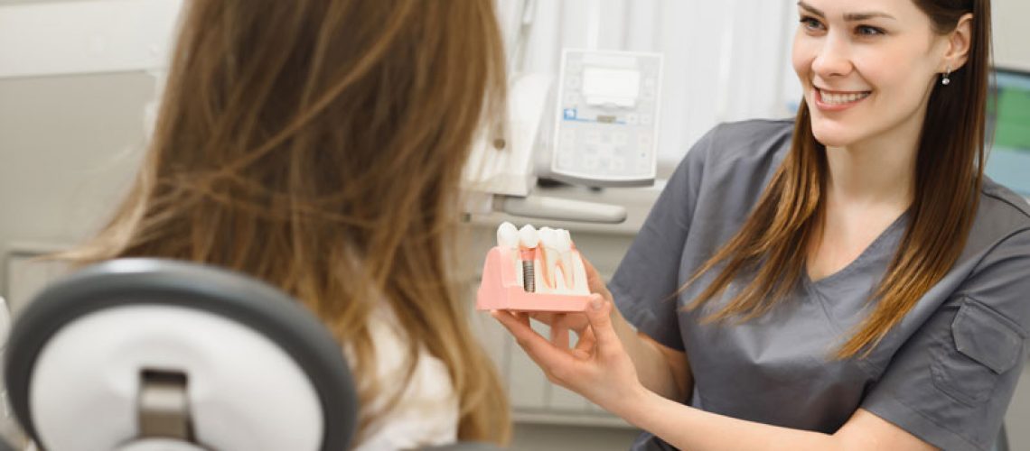 a happy doctor showing a candidate for dental implants a dental implant model before her procedure begins.