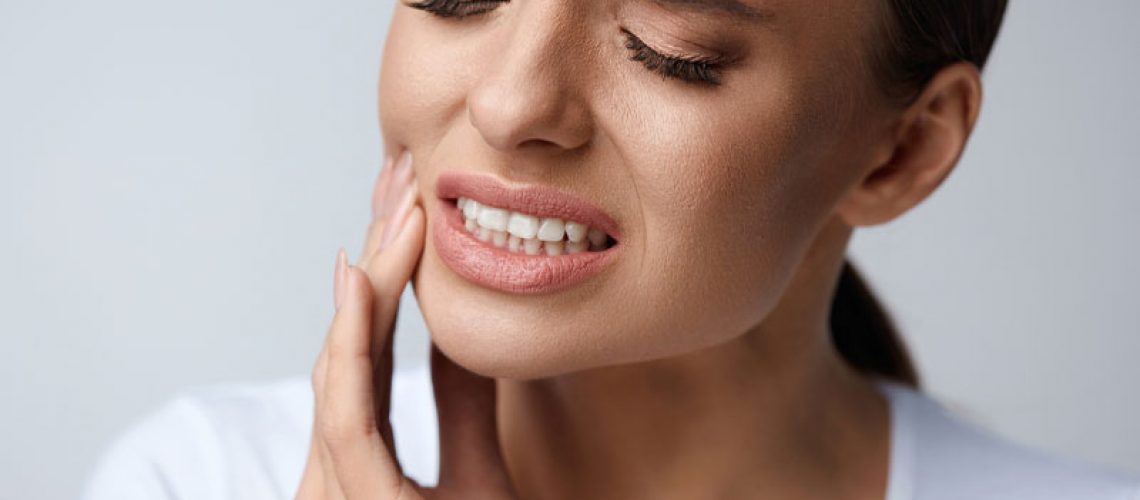 a woman who is wincing and holding the side of her jaw in pain because she has a problematic wisdom tooth.