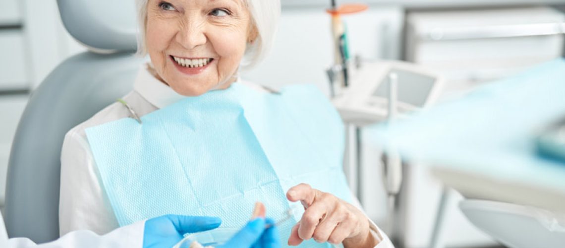 An image of an older woman sitting in a dental chair after a dental implant procedure.